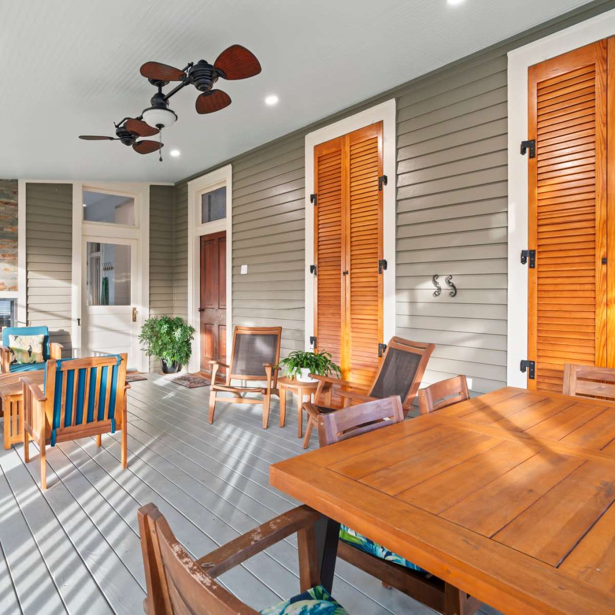 A spacious screened porch featuring wooden furniture, a ceiling fan, and decorative shuttered windows.