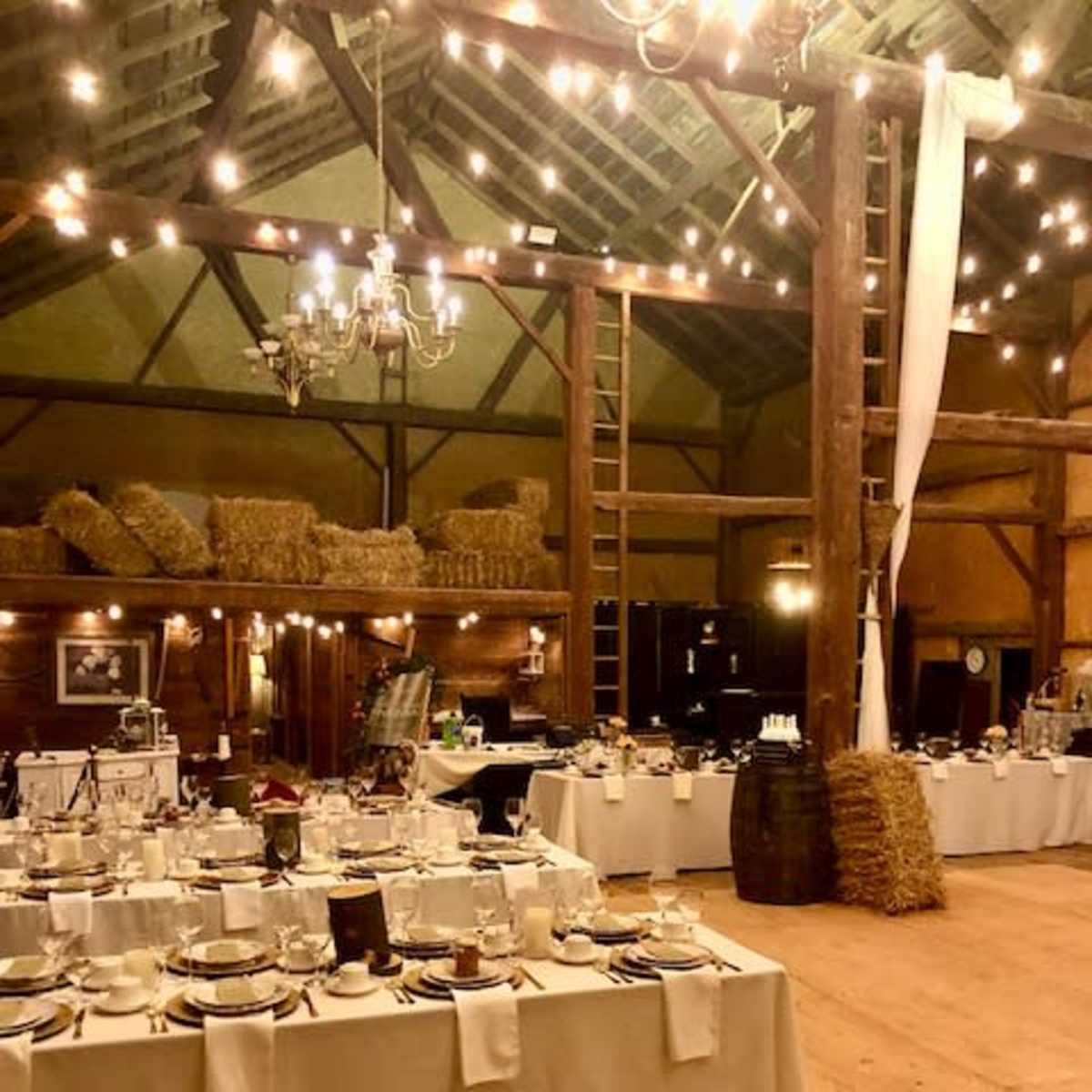 A rustic banquet hall with elegantly set tables, string lights, and wooden beams.