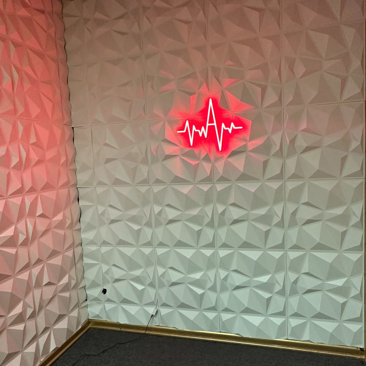 A corner of a room featuring a textured white wall and a red neon heartbeat sign.