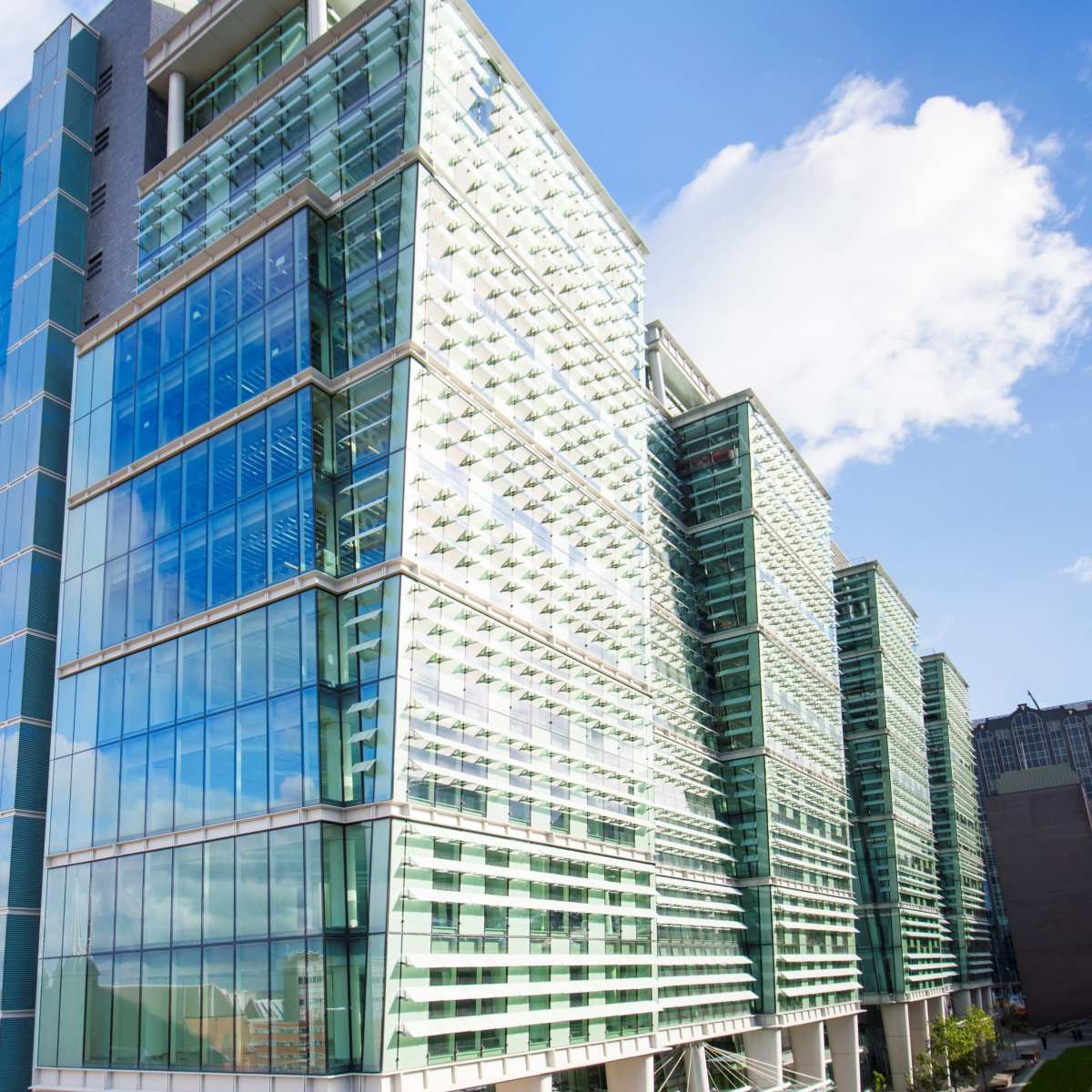 A modern glass and steel building with multiple stories reflects the sky in its windows.