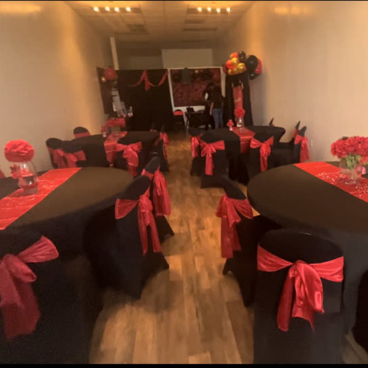 A decorated event space with black tables draped in red table runners and black chairs adorned with red bows.