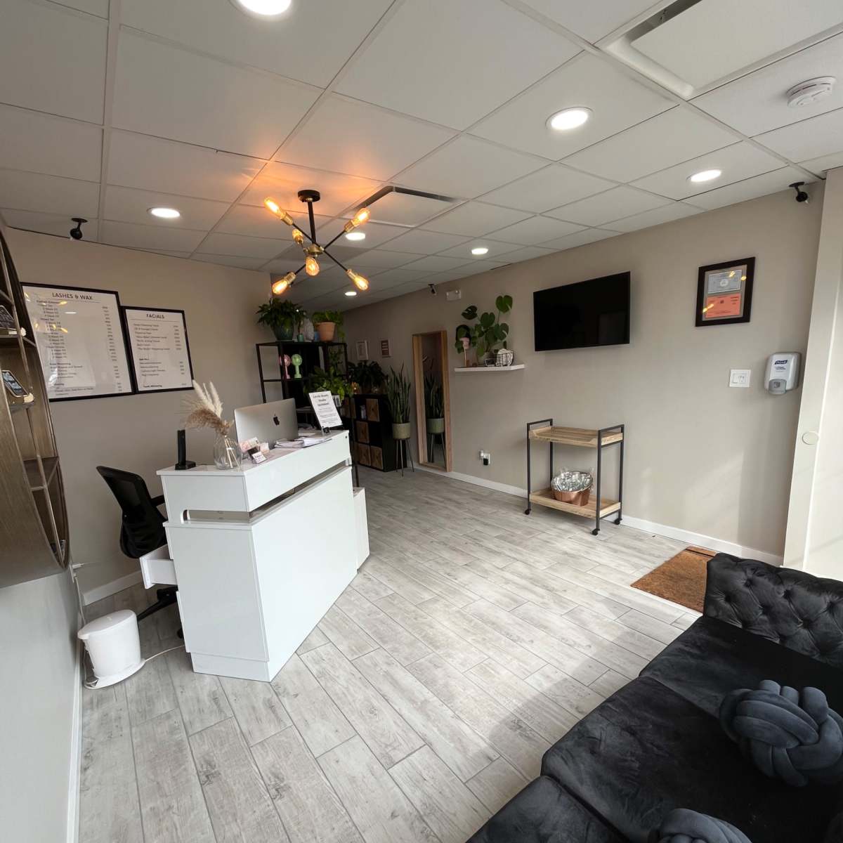 A modern reception area featuring a white front desk, a black sofa, and wall-mounted decoration in a well-lit space.