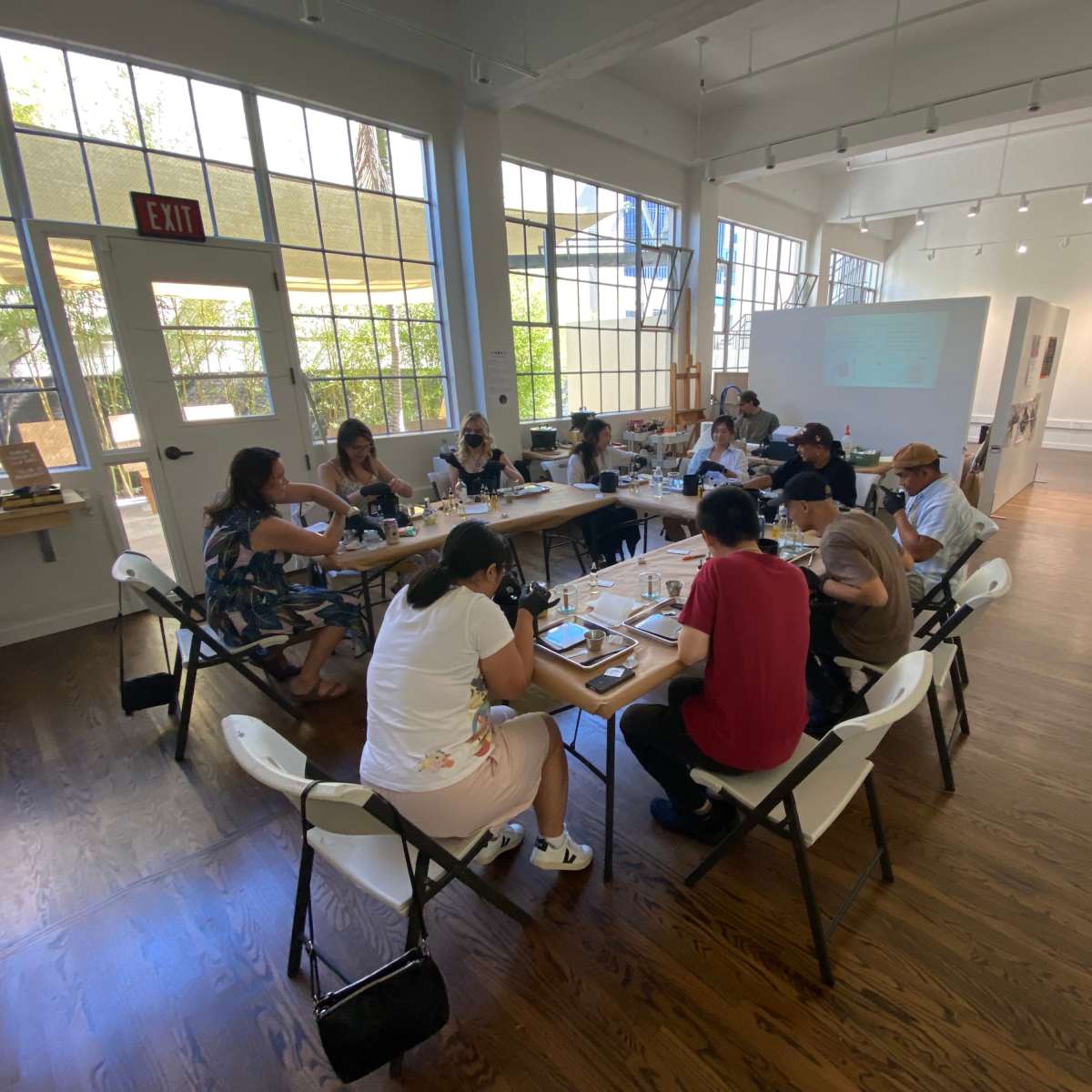A group of people is gathered around a large table in a brightly lit room, engaged in a collaborative activity.