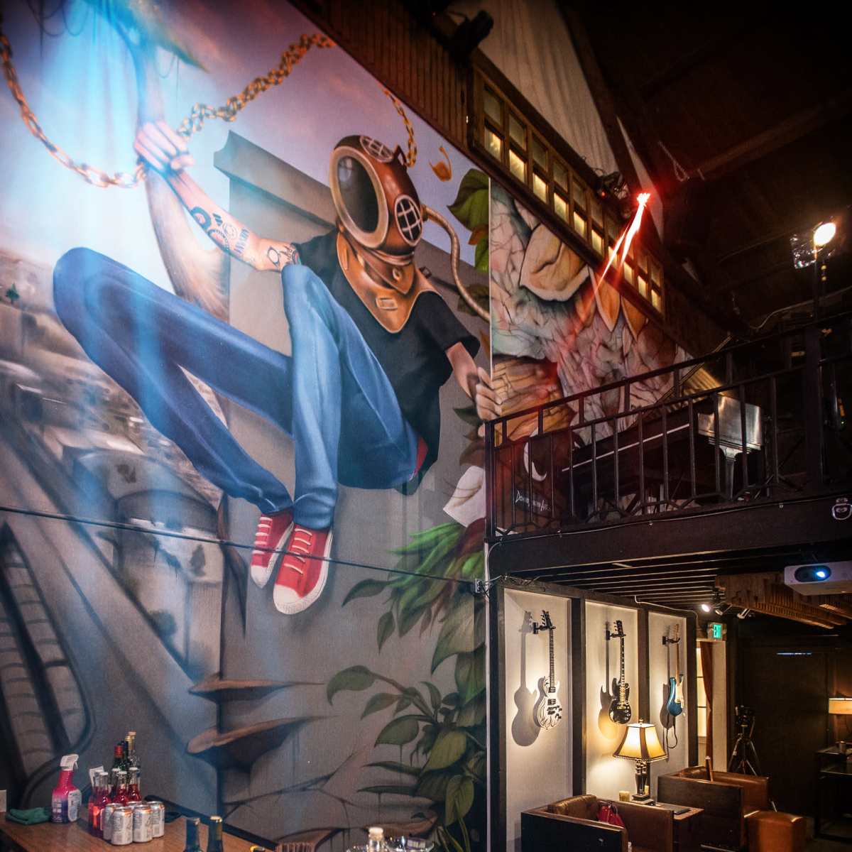 The scene features a bar area with a wooden counter displaying various bottles and glasses, alongside a colorful mural of a figure in a helmet, and a wall adorned with guitars in a dimly lit venue.