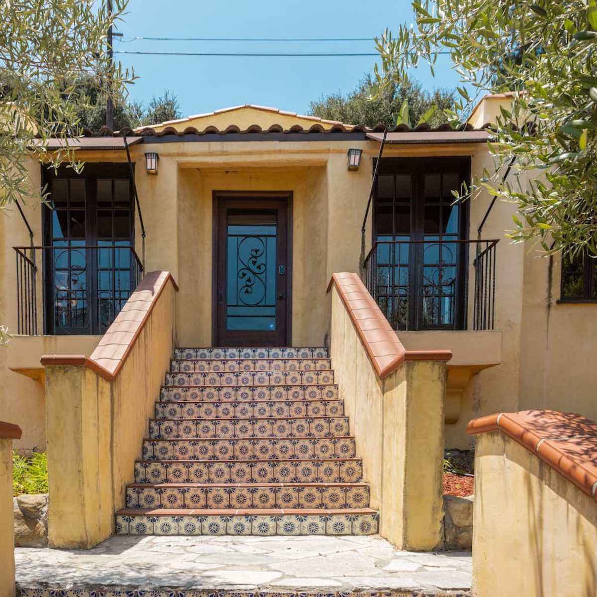 A textured yellow house with a prominent door, framed by two large windows and featuring a decorative tiled staircase leading up to the entrance.