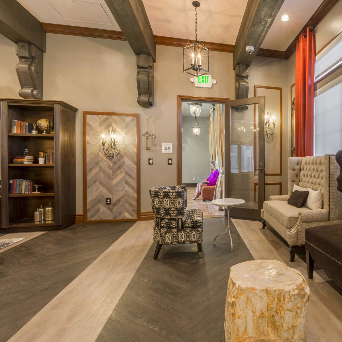 A cozy lounge area featuring two upholstered sofas, a small table, a decorative wooden stool, and bookshelves in a well-lit room with elegant curtains and modern lighting fixtures.