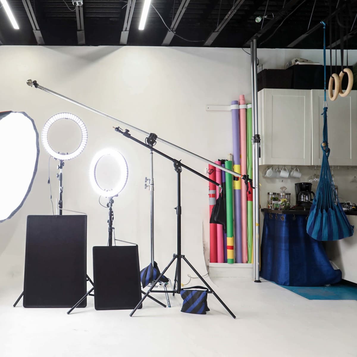 A photography studio setup featuring three lighting fixtures, two light stands, a backdrop, and colorful props arranged along the wall.