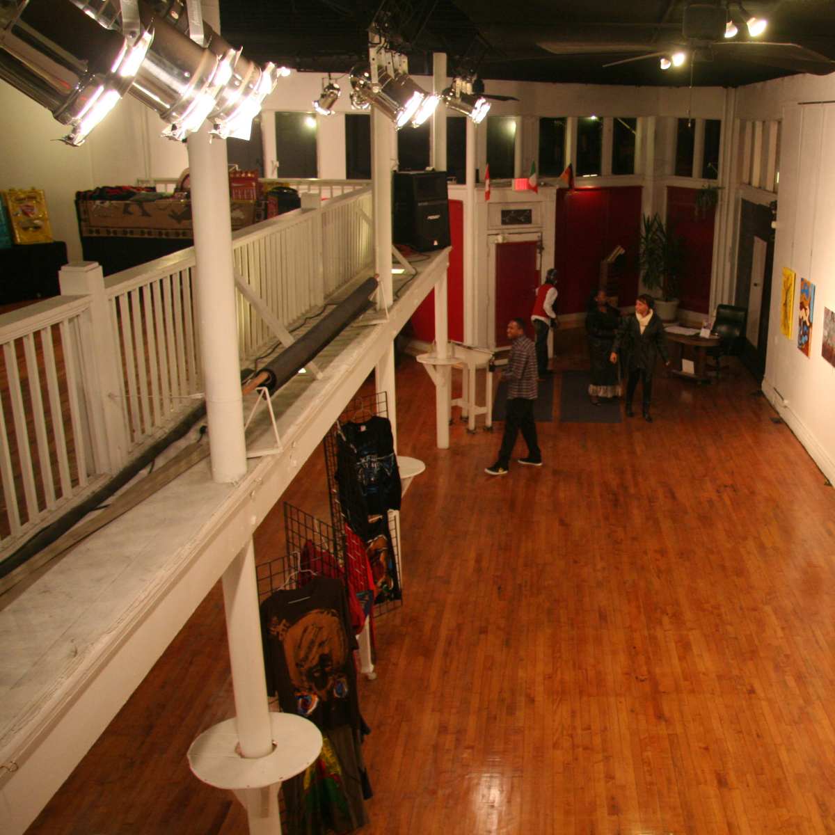 A spacious art gallery with polished wooden floors, featuring various artworks hanging on the walls and two individuals interacting in the center of the room.
