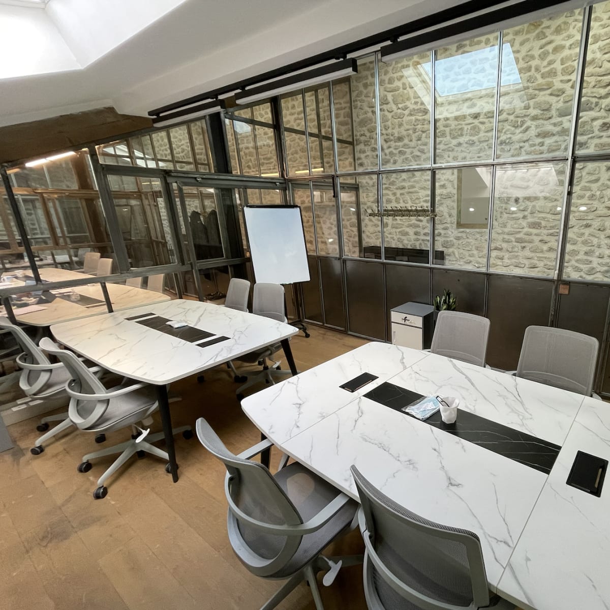 A modern conference room with large marble-topped tables, ergonomic chairs, and glass walls featuring exposed stone.