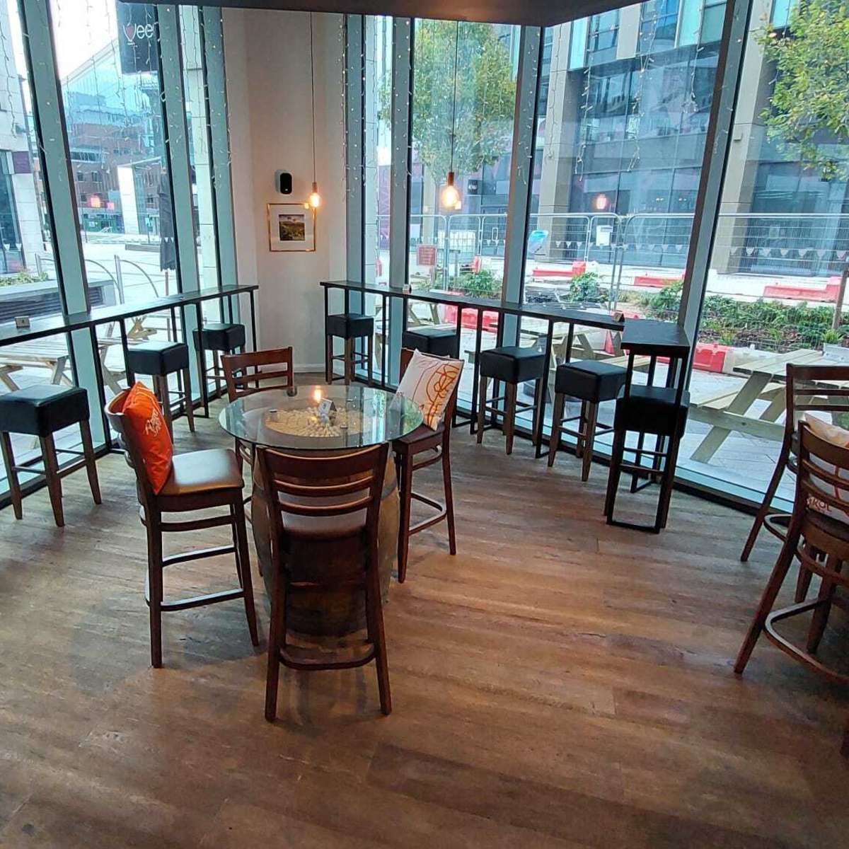 A modern café interior with tall chairs surrounding a circular glass table and large windows overlooking an outdoor space.