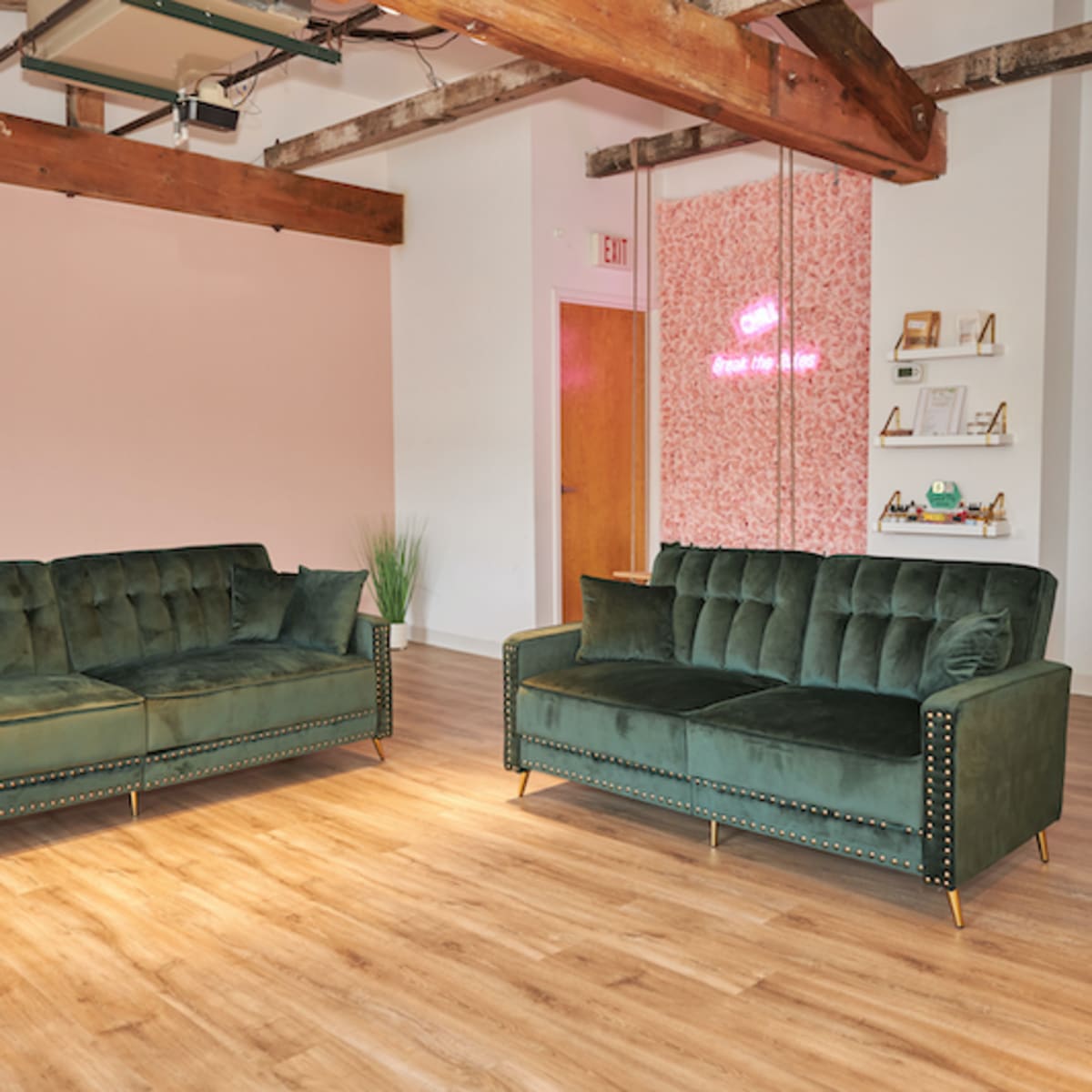 Two green velvet sofas positioned facing each other in a brightly lit room with wooden beams and a pink wall.
