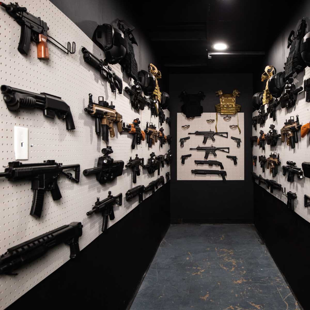 A narrow hallway lined with various firearms displayed on pegboards against black walls.