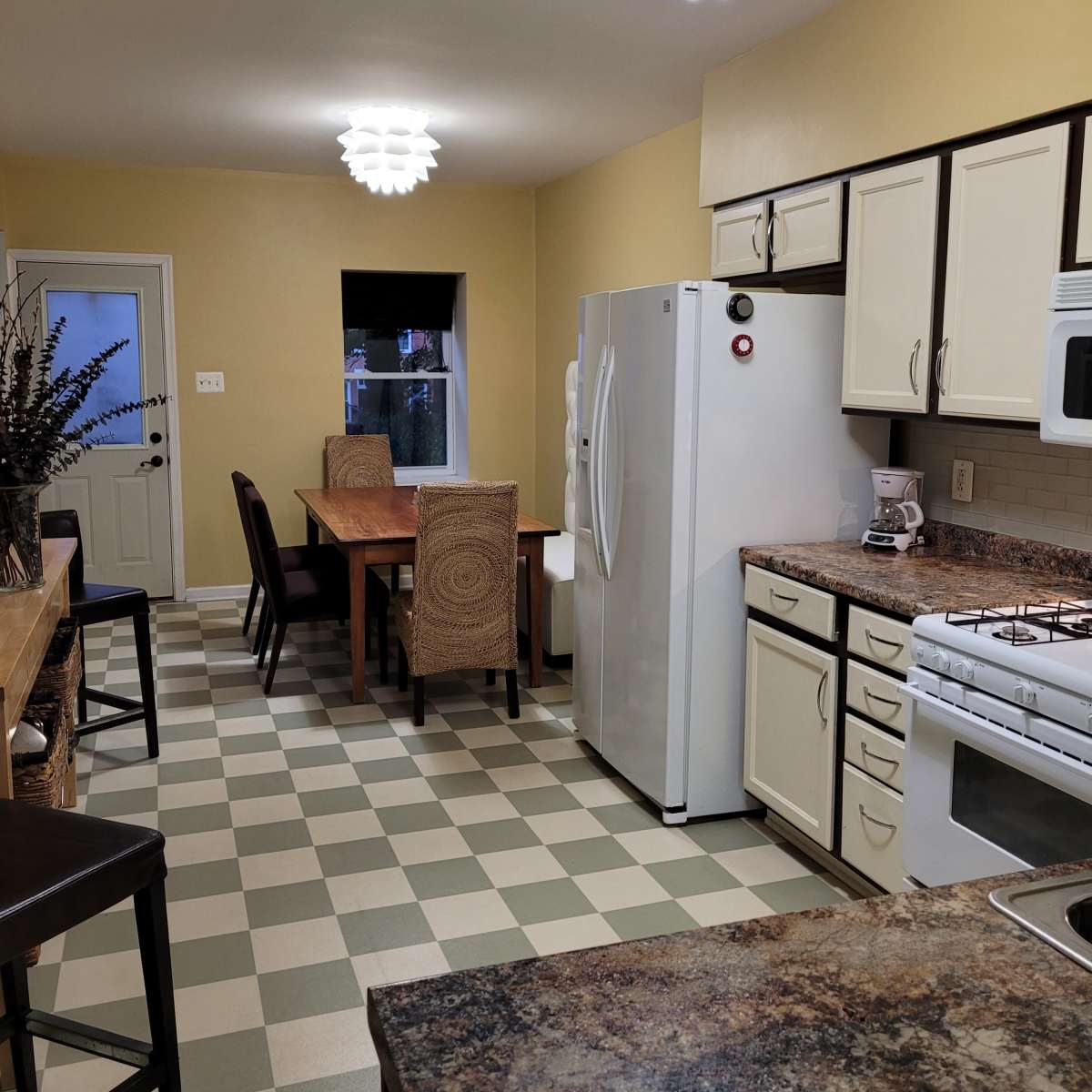A kitchen features a dining table with chairs, a white refrigerator, and a stove, all illuminated by modern pendant lights.