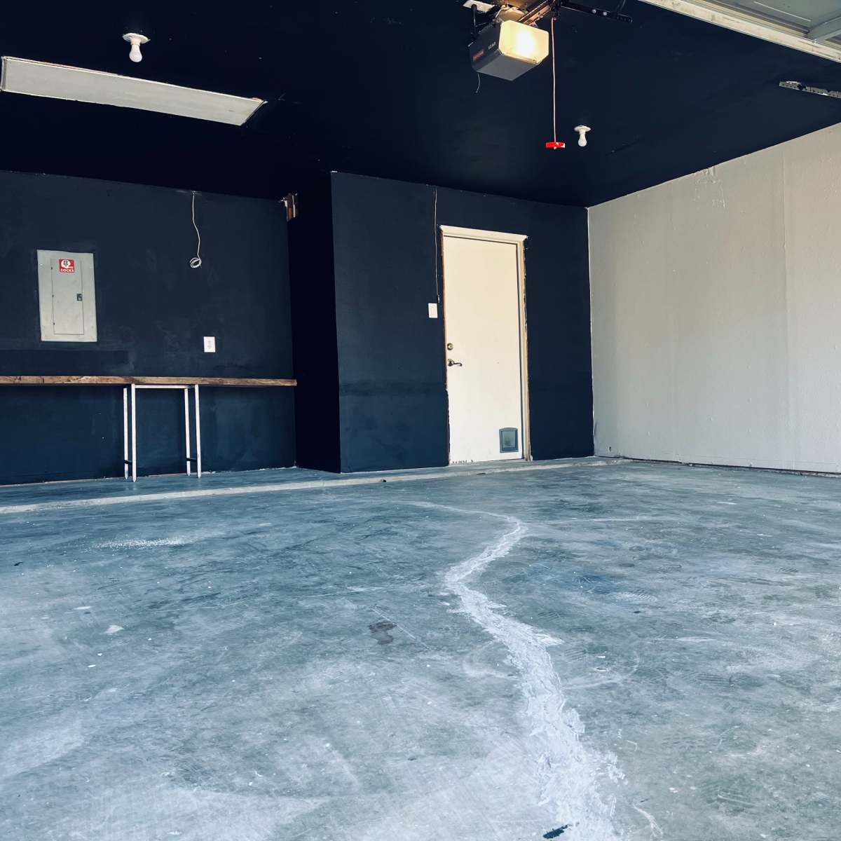 An empty garage featuring a concrete floor, a closed door, and walls painted in two colors, black and grey.