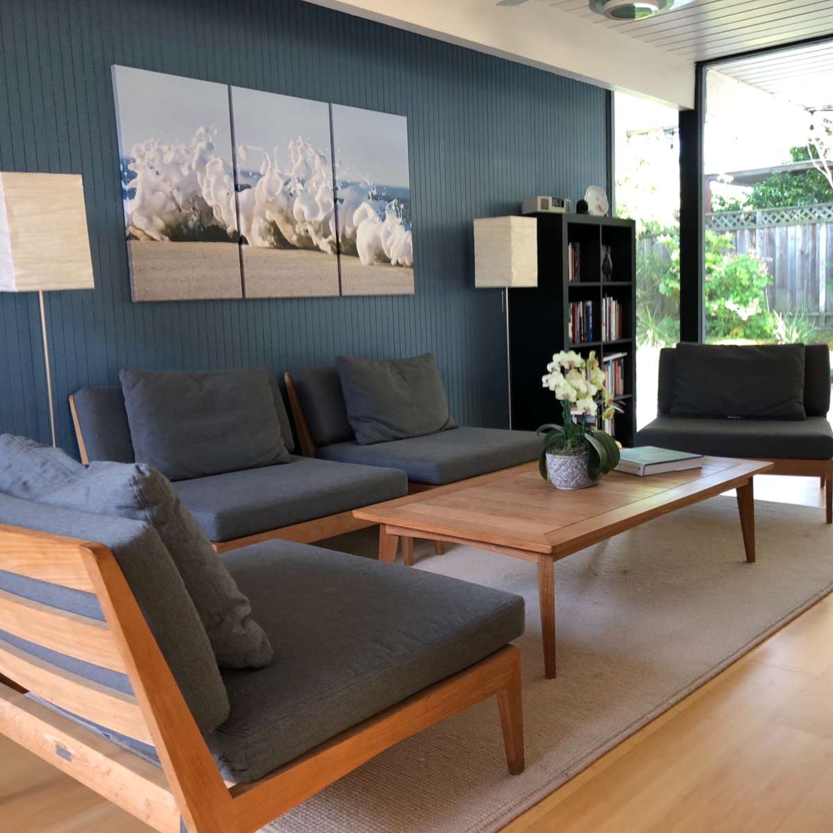 A modern living room features gray sofas, a wooden coffee table, and large windows overlooking a garden.