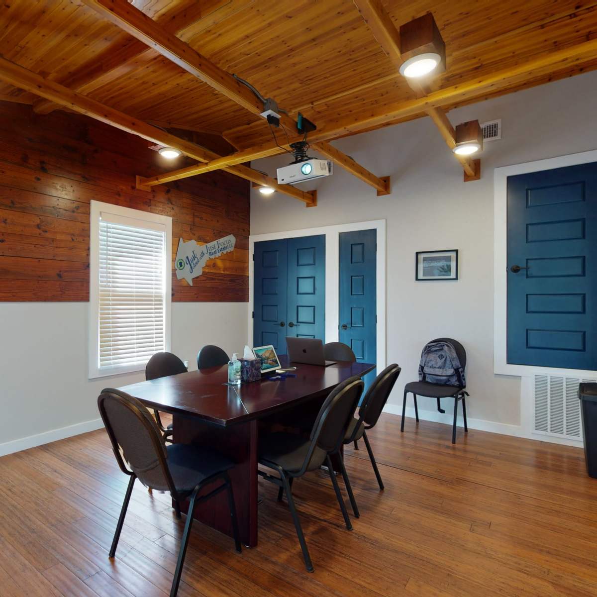 A meeting room with a wooden ceiling, a large table surrounded by chairs, and blue doors against a wooden wall.
