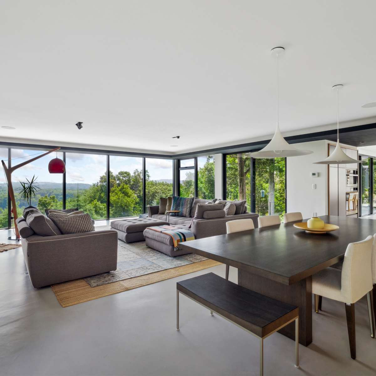 A modern living space with a seating area featuring large windows overlooking a green landscape and a dining table with chairs.