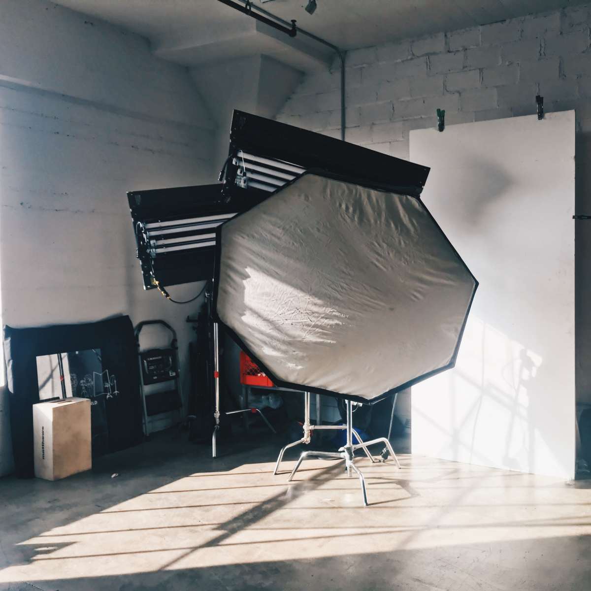 A large octagonal softbox is positioned in a well-lit photography studio with a white backdrop and a storage unit.