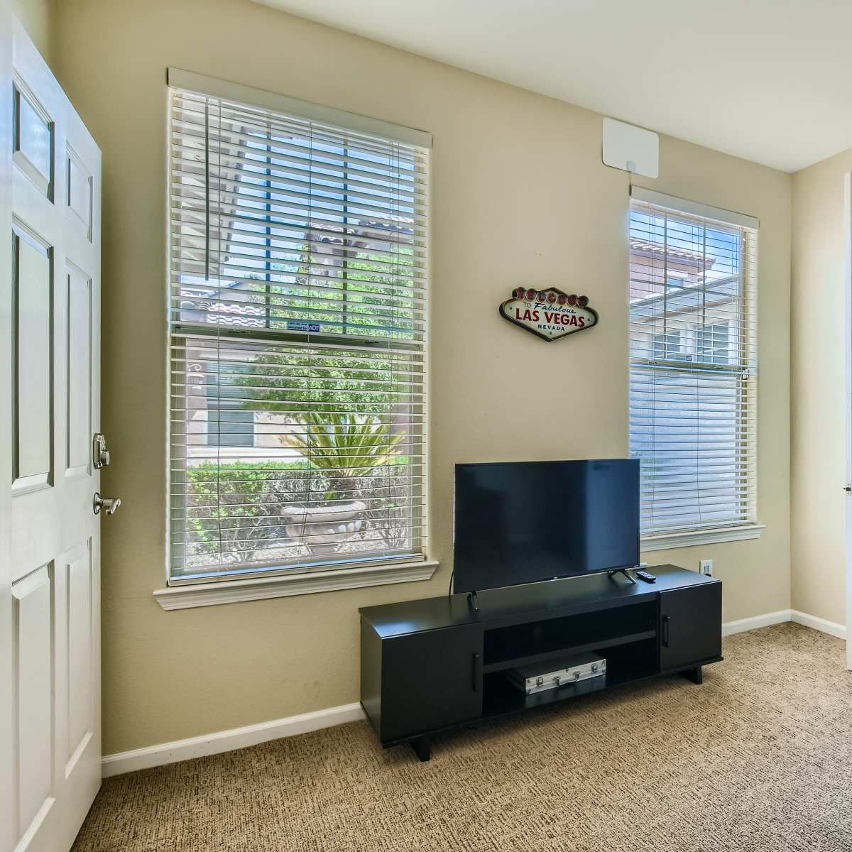 An entryway with two windows, a television on a black stand, and a door leading to another room.