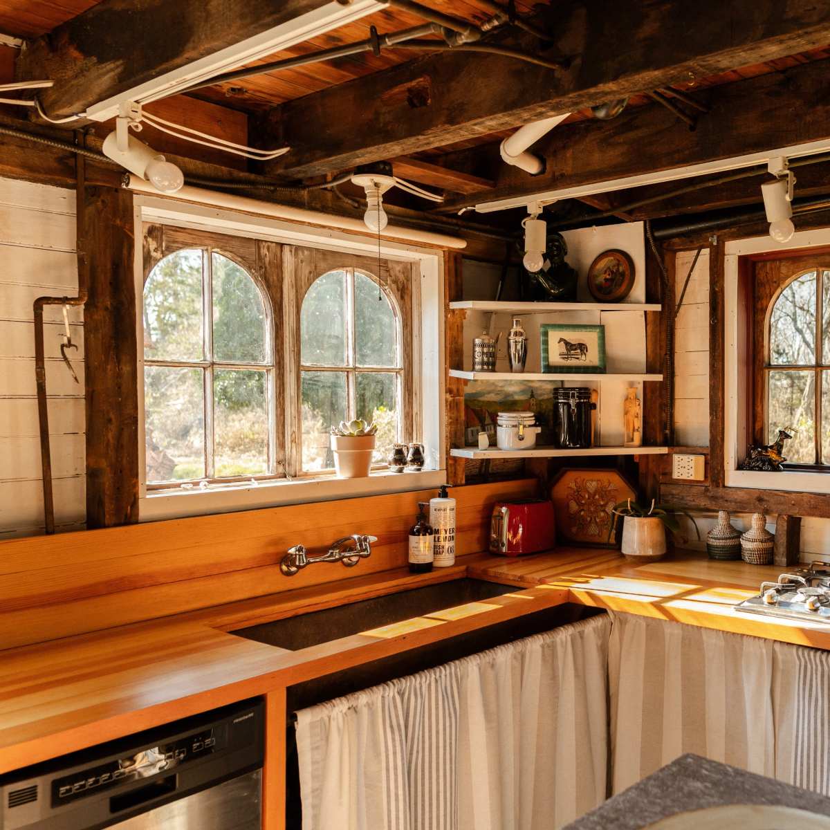 A rustic kitchen featuring wooden countertops, a gas stove, and two arched windows with natural light streaming in.