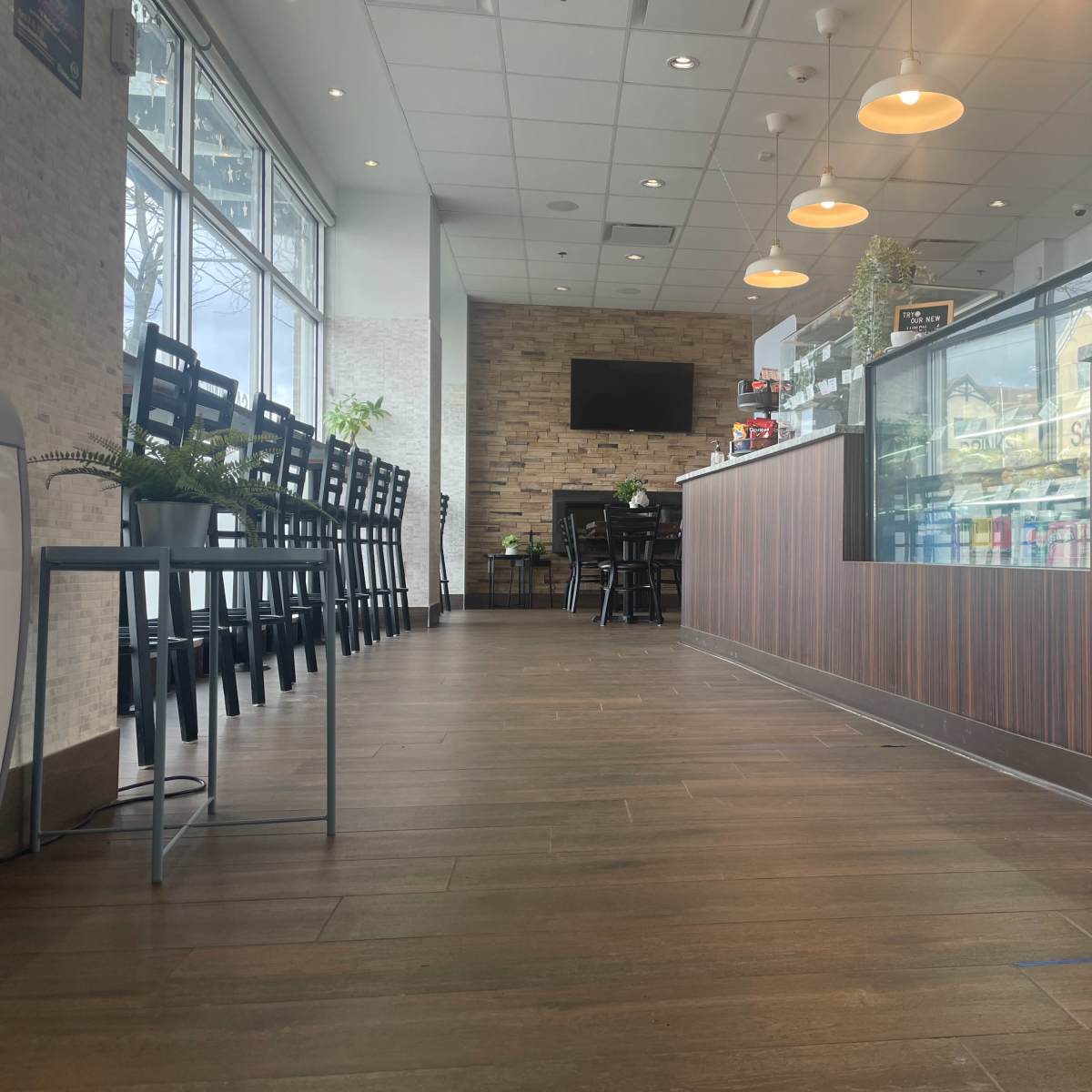 A modern café interior with a wooden counter, empty seating, and a television on the wall.