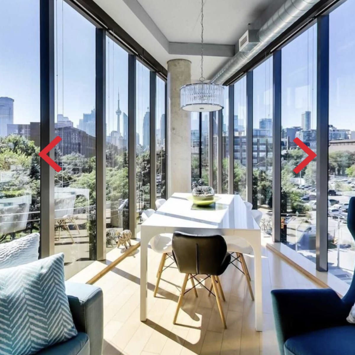 A bright, modern dining area features a white table, black chairs, and large windows offering a view of a city skyline.