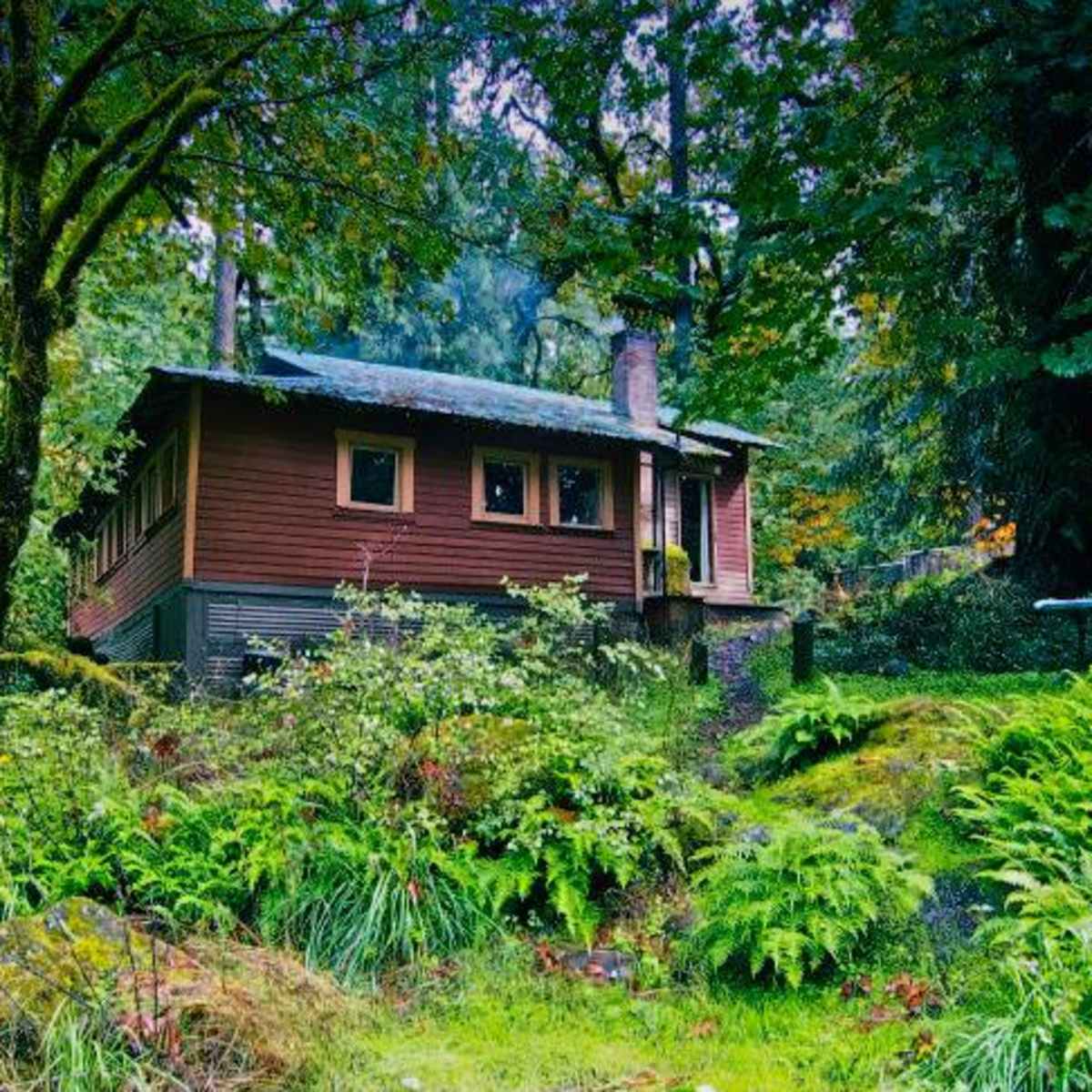 A brown cottage is nestled among lush green foliage in a forested area.