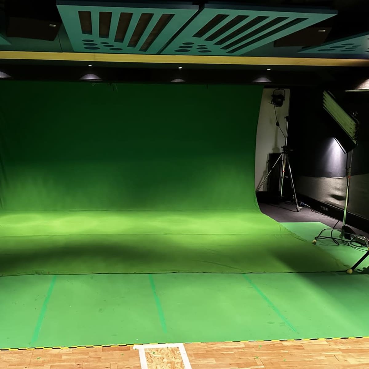 A studio setup featuring a large green screen, with lighting equipment positioned on either side.