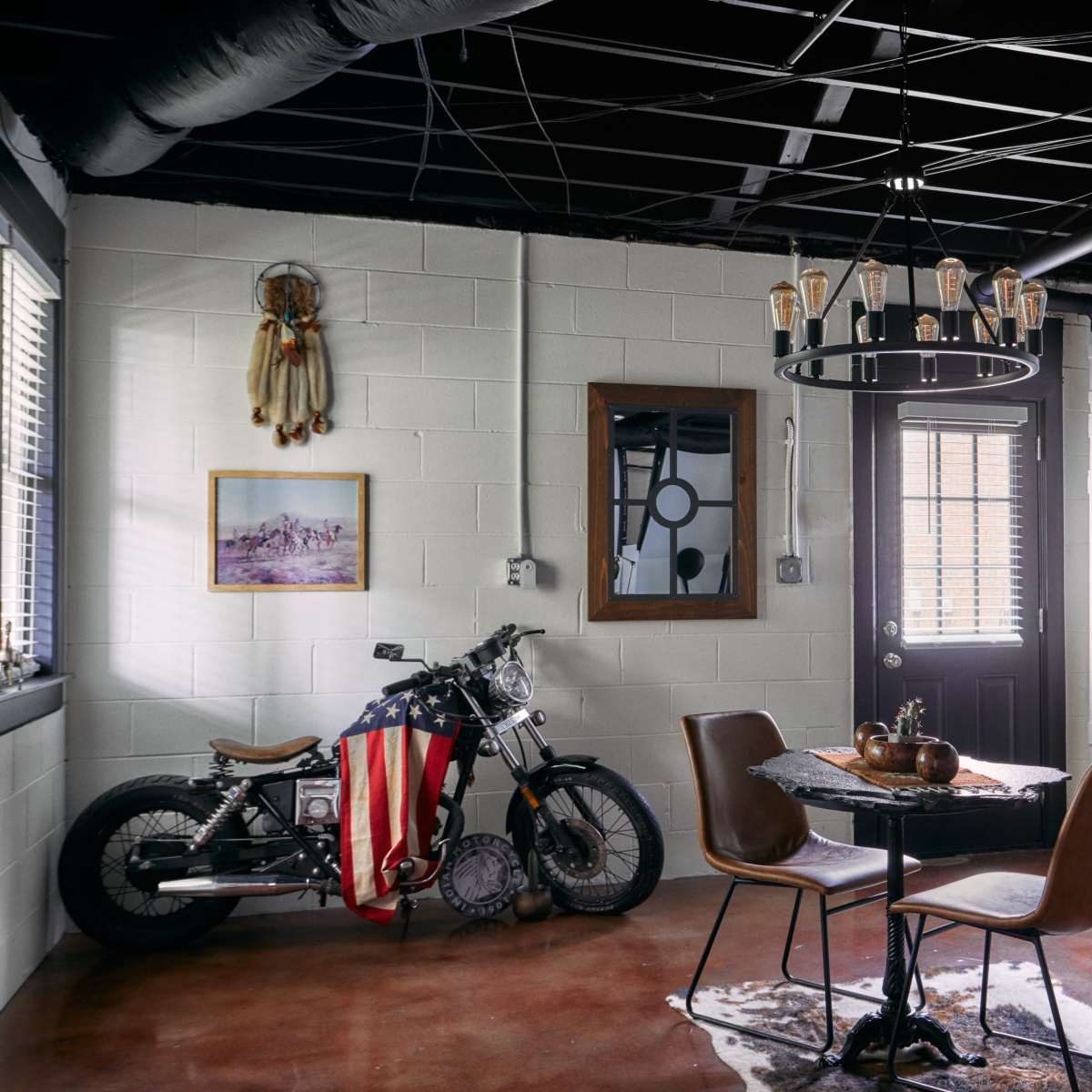The room features a motorcycle draped with an American flag, a round dining table with chairs, and various wall decorations including artwork and a mirror.