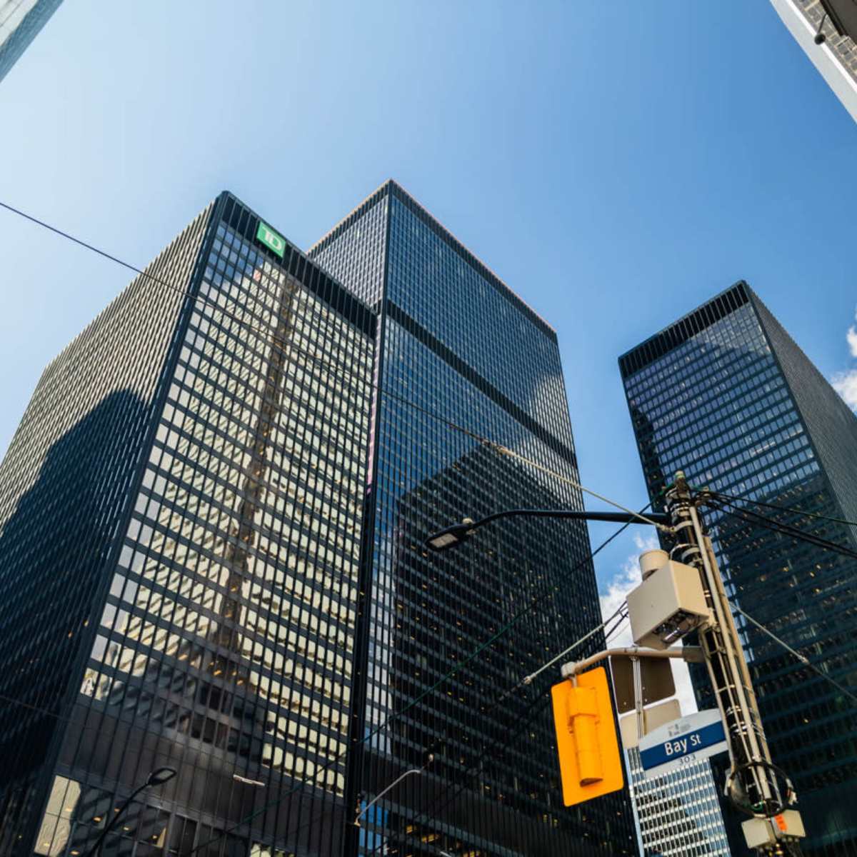 A view of tall glass skyscrapers against a blue sky with clouds, viewed from street level.