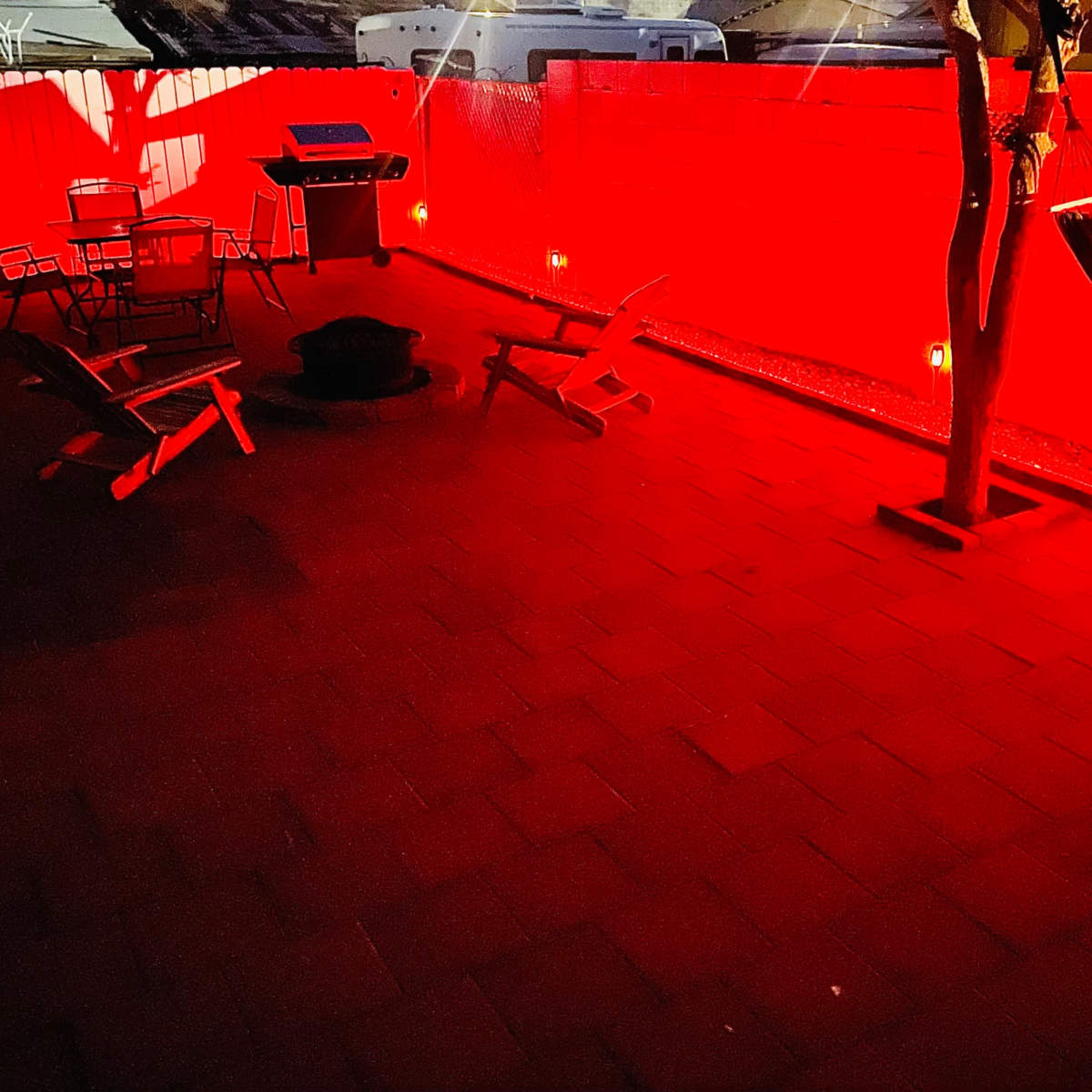 A patio area features a grill, seating, and a hammock, all illuminated by red lights against a contrasting wall.
