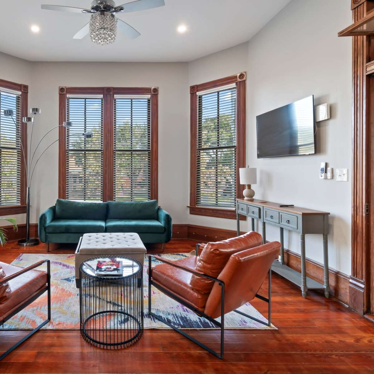 A living room features a green sofa, two brown chairs, a coffee table, and large windows with blinds.