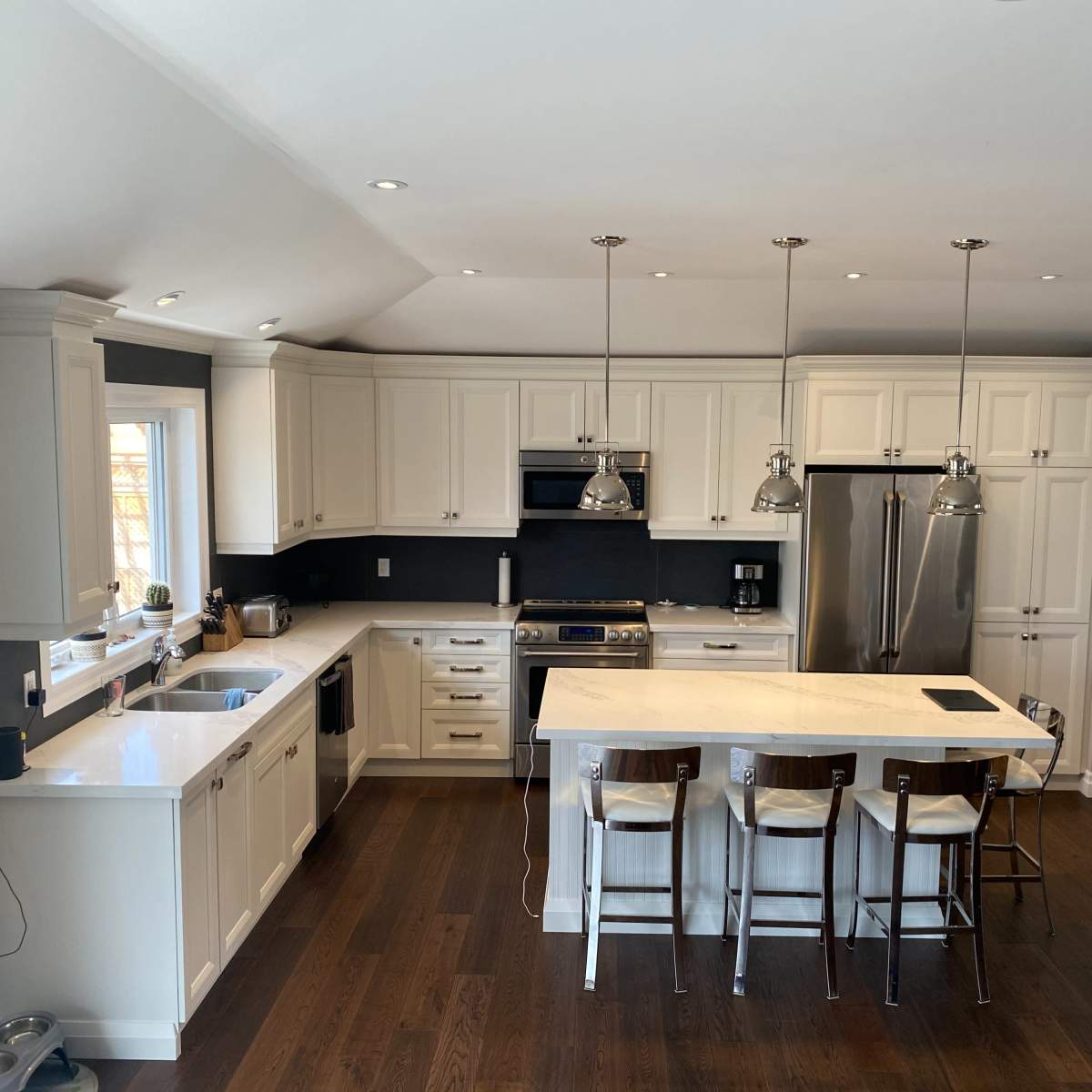 The modern kitchen features white cabinetry, a central island with seating, stainless steel appliances, and hardwood flooring.