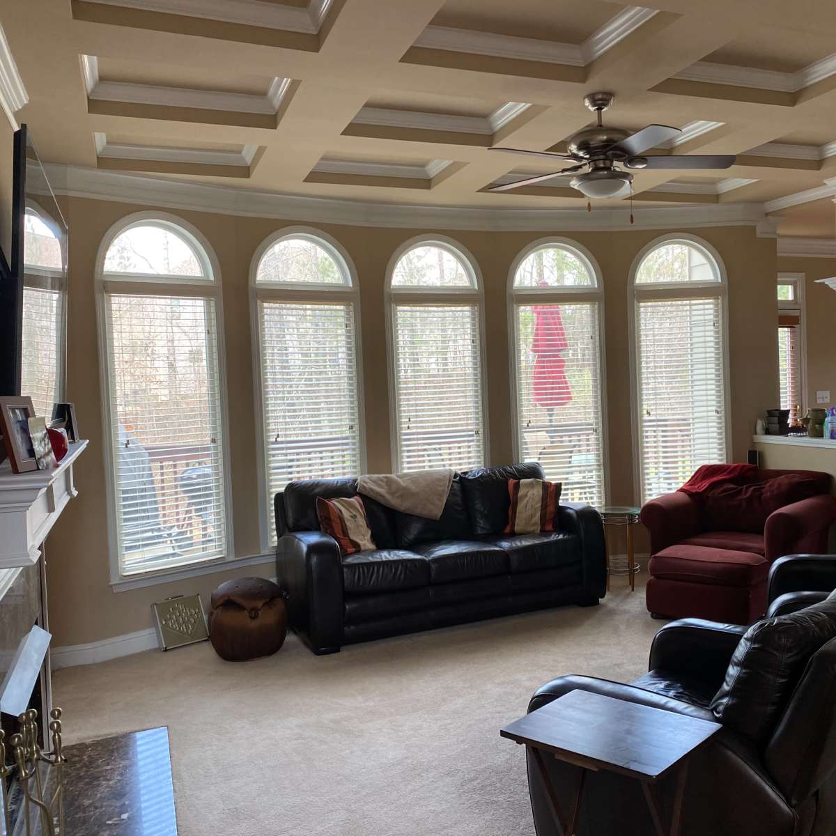 A spacious living room with a coffered ceiling, large arched windows, and a mix of black leather and red upholstered furniture.