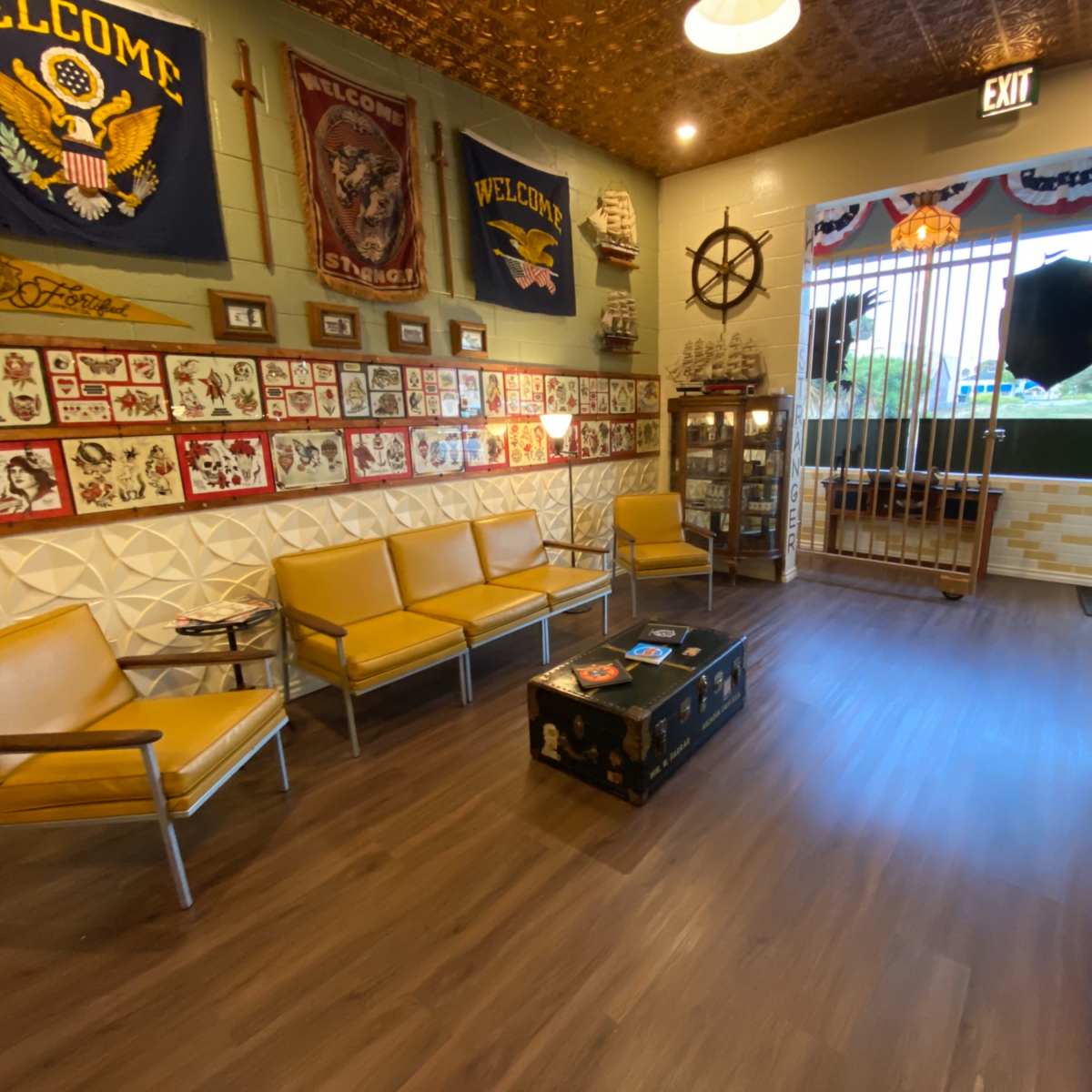 The interior of the room features a seating area with yellow chairs and a wooden coffee table, surrounded by framed art and decorative flags.