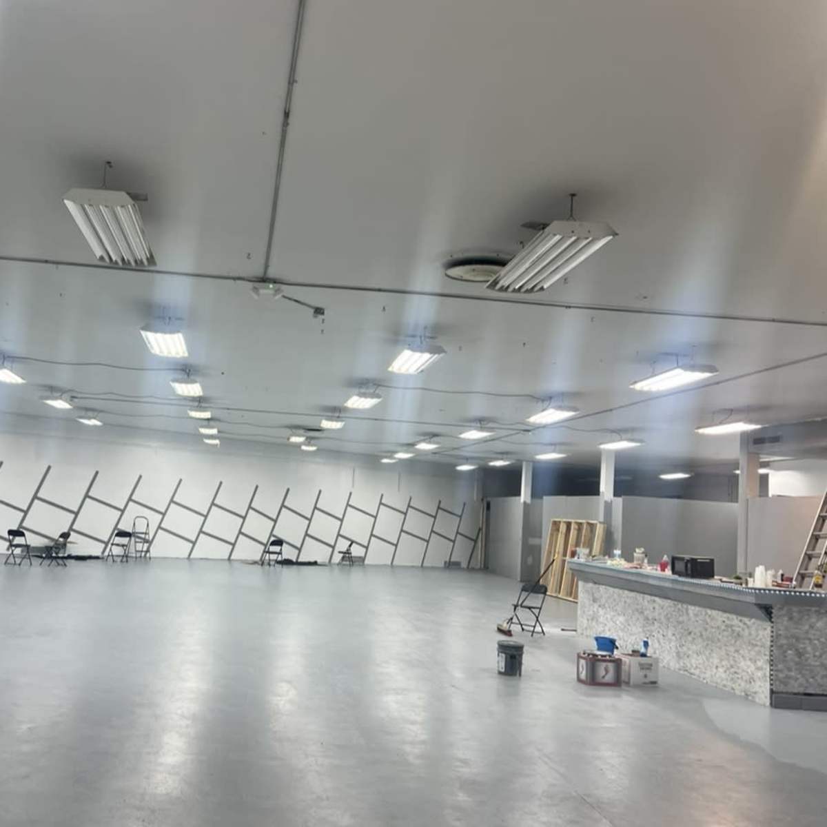 A large, empty interior space with a polished concrete floor, bright fluorescent lights, and a wall featuring diagonal black stripes.