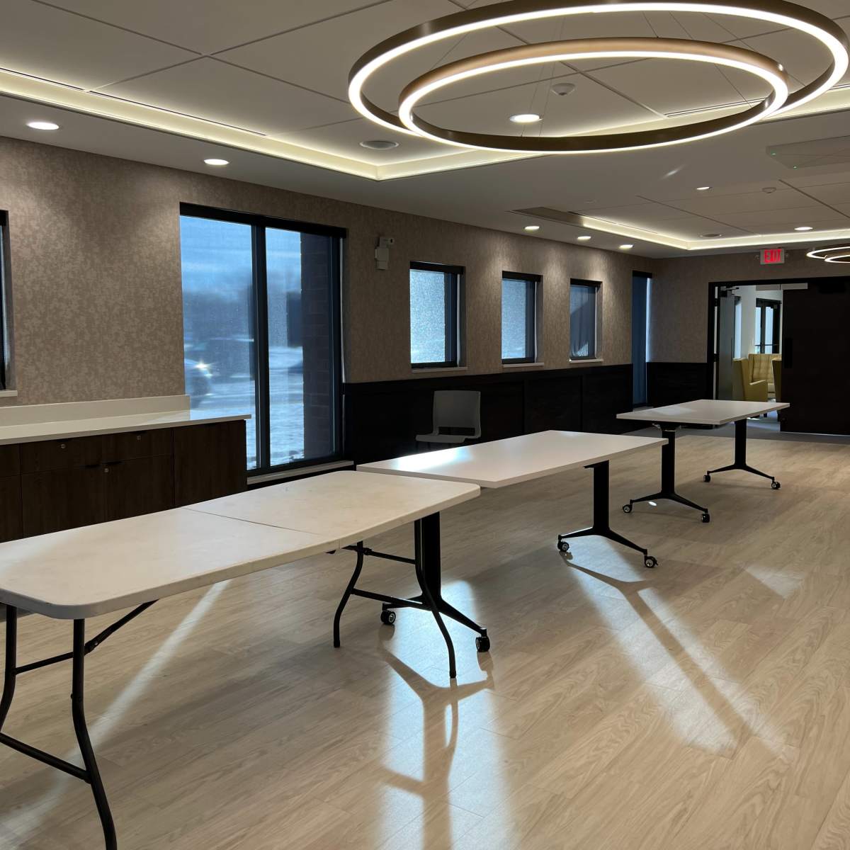 A modern room with several folding tables arranged in a row, accompanied by large windows that allow natural light to enter.