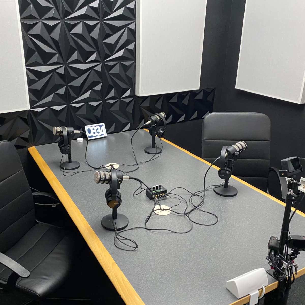 A quiet recording studio features a table with four microphones, two chairs, and soundproof wall panels.