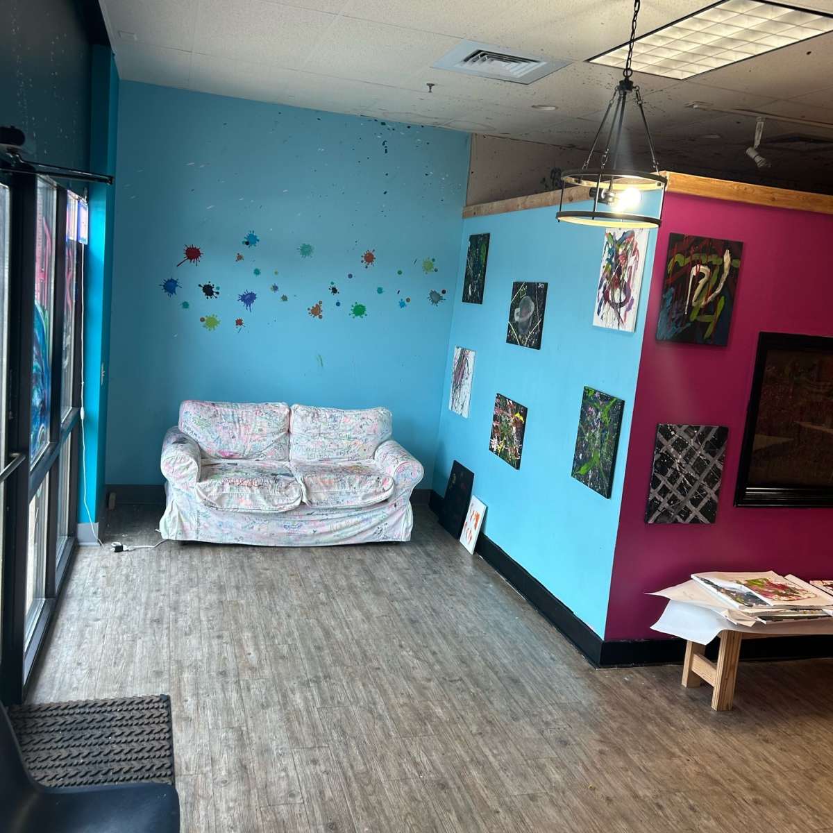 A room with a colorful blue and pink wall, a patterned couch, and several pieces of artwork displayed on the walls.