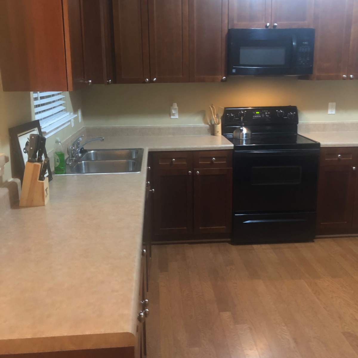 The kitchen features wooden cabinets, a black stove, and a stainless steel sink with a countertop made of beige material.