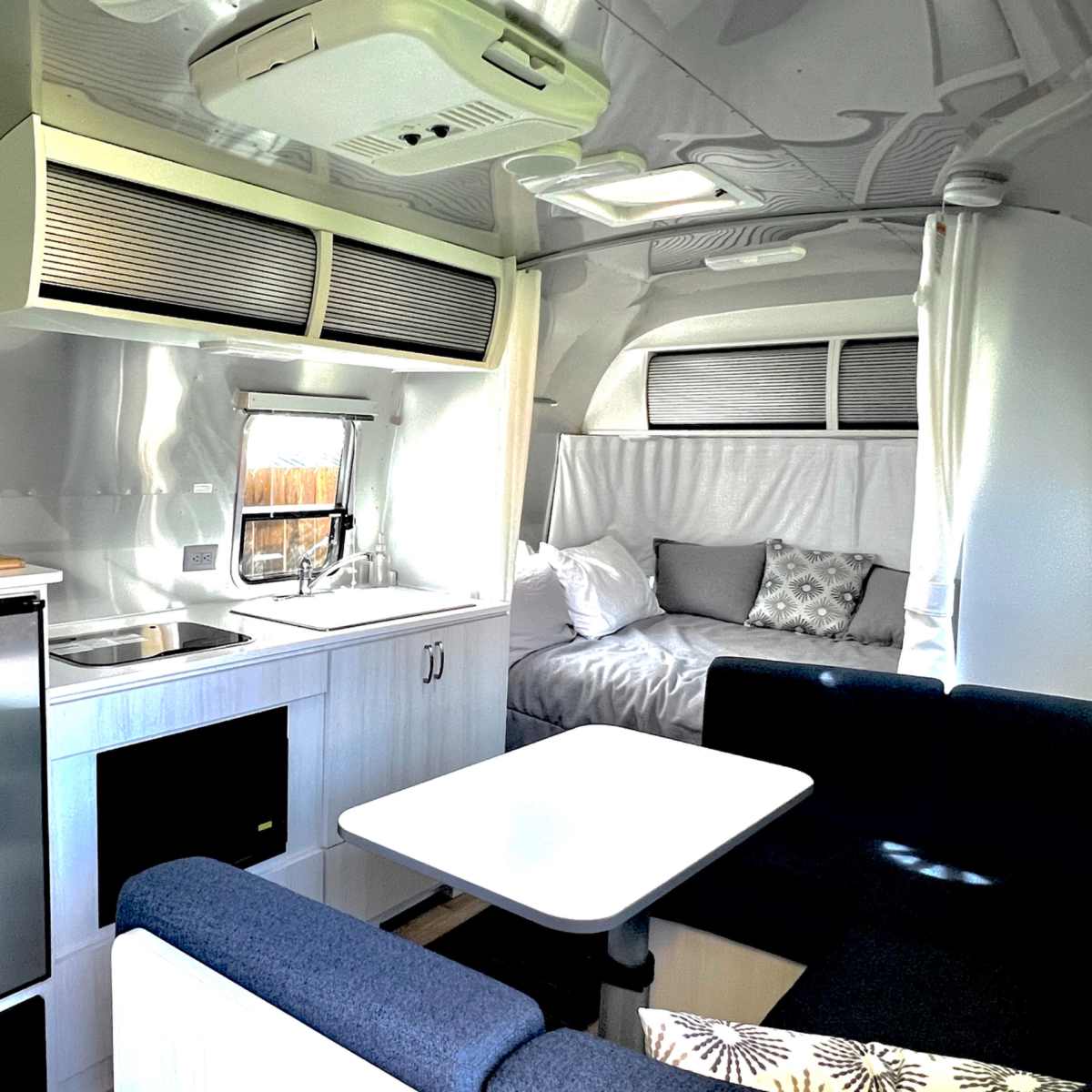 The interior of a modern camper trailer featuring a kitchenette, a dining area, and a sleeping space.