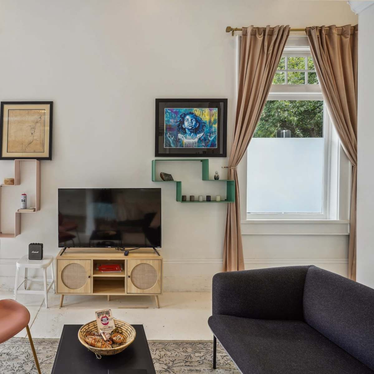 A modern living room with a television on a wooden stand, pink and gray chairs, and decorative shelves on the wall.