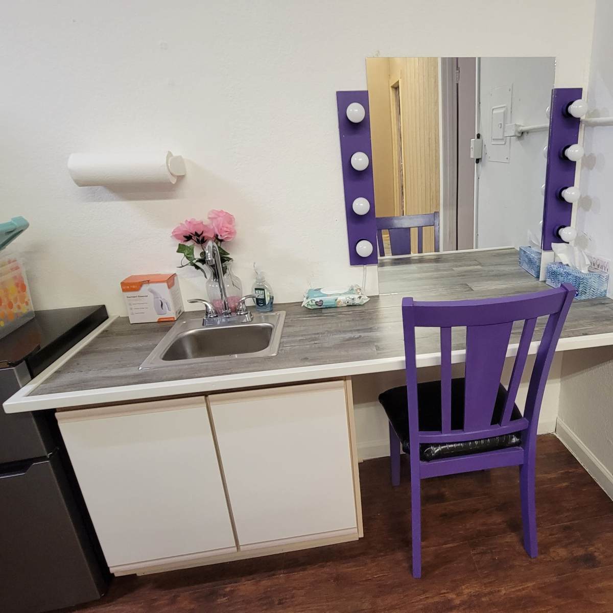 A small vanity area with a mirror, a sink, a chair, and various beauty products neatly arranged on the counter.
