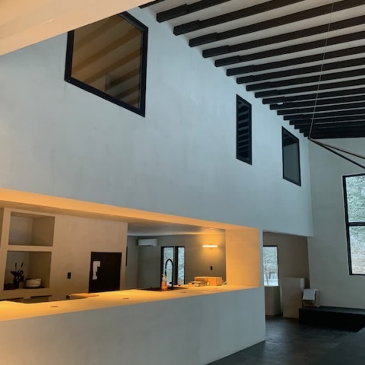 An interior of a modern space featuring high ceilings, exposed wooden beams, and large windows that allow light to enter.
