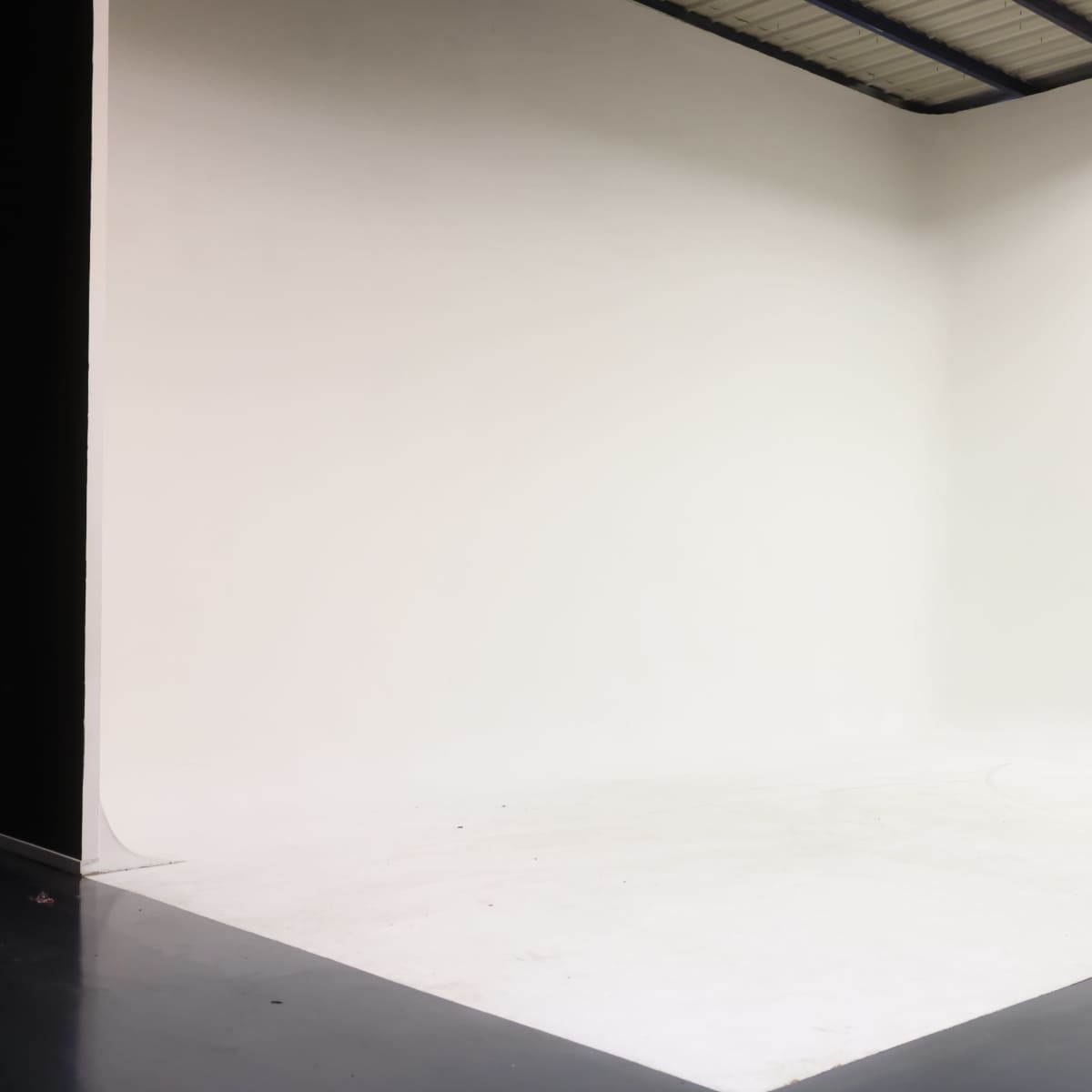 A large, empty studio space with a seamless white backdrop and a polished dark floor.