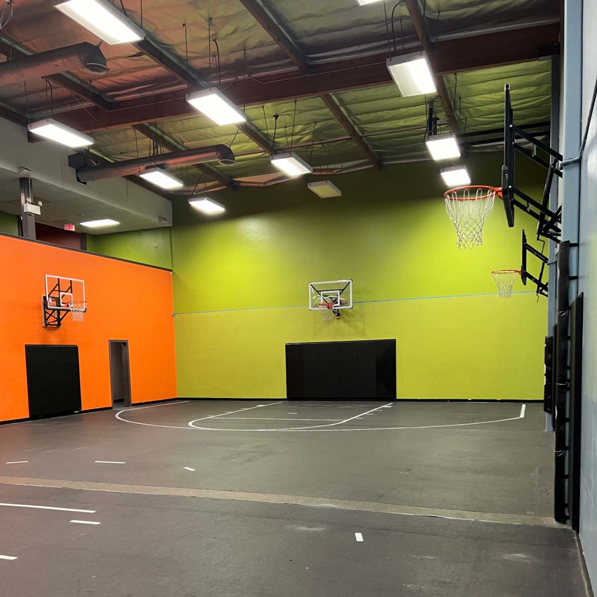A basketball court with two hoops at either end, surrounded by brightly colored walls in orange and green.