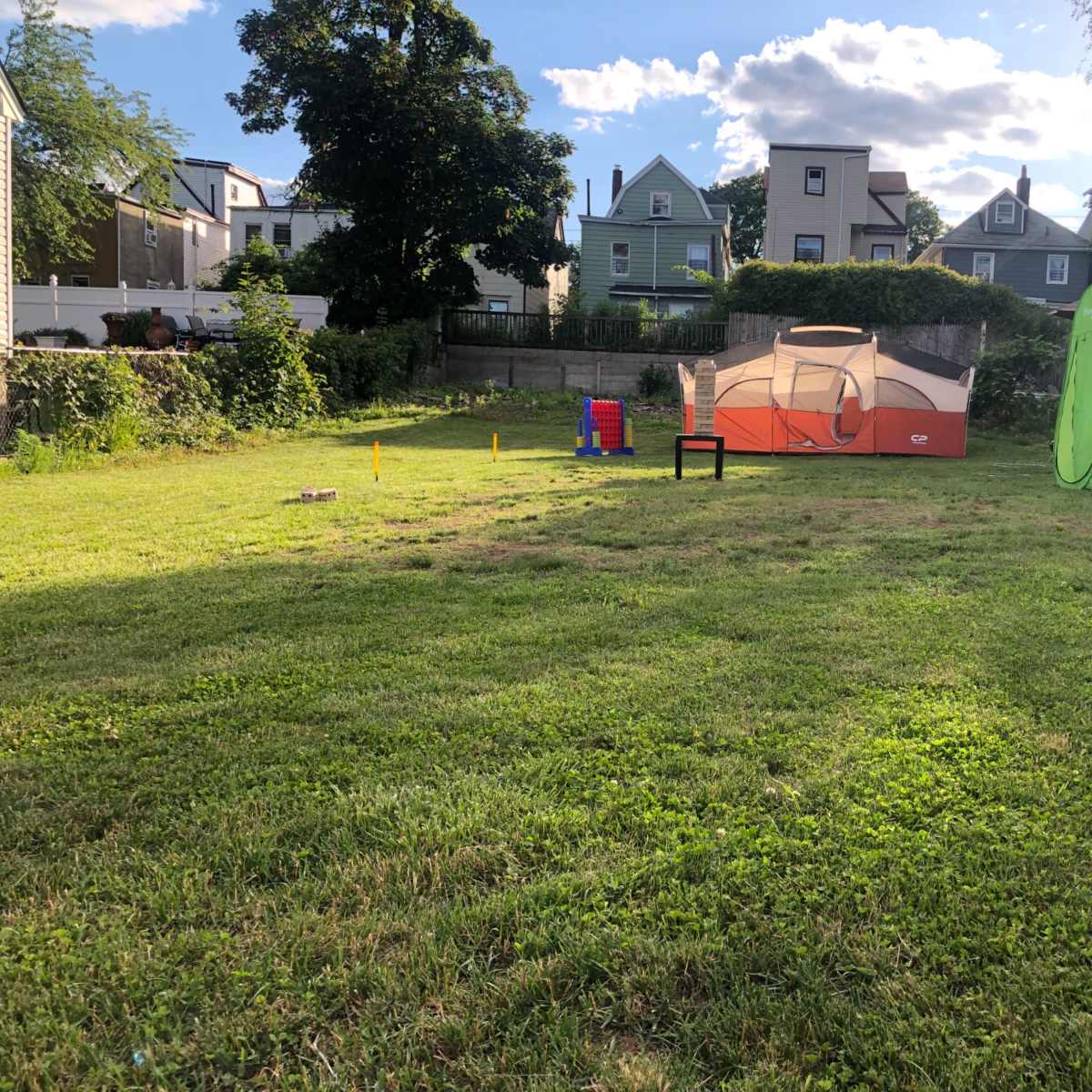 A grassy backyard with a tent, a folding chair, and a portable changing room set up in the open area.