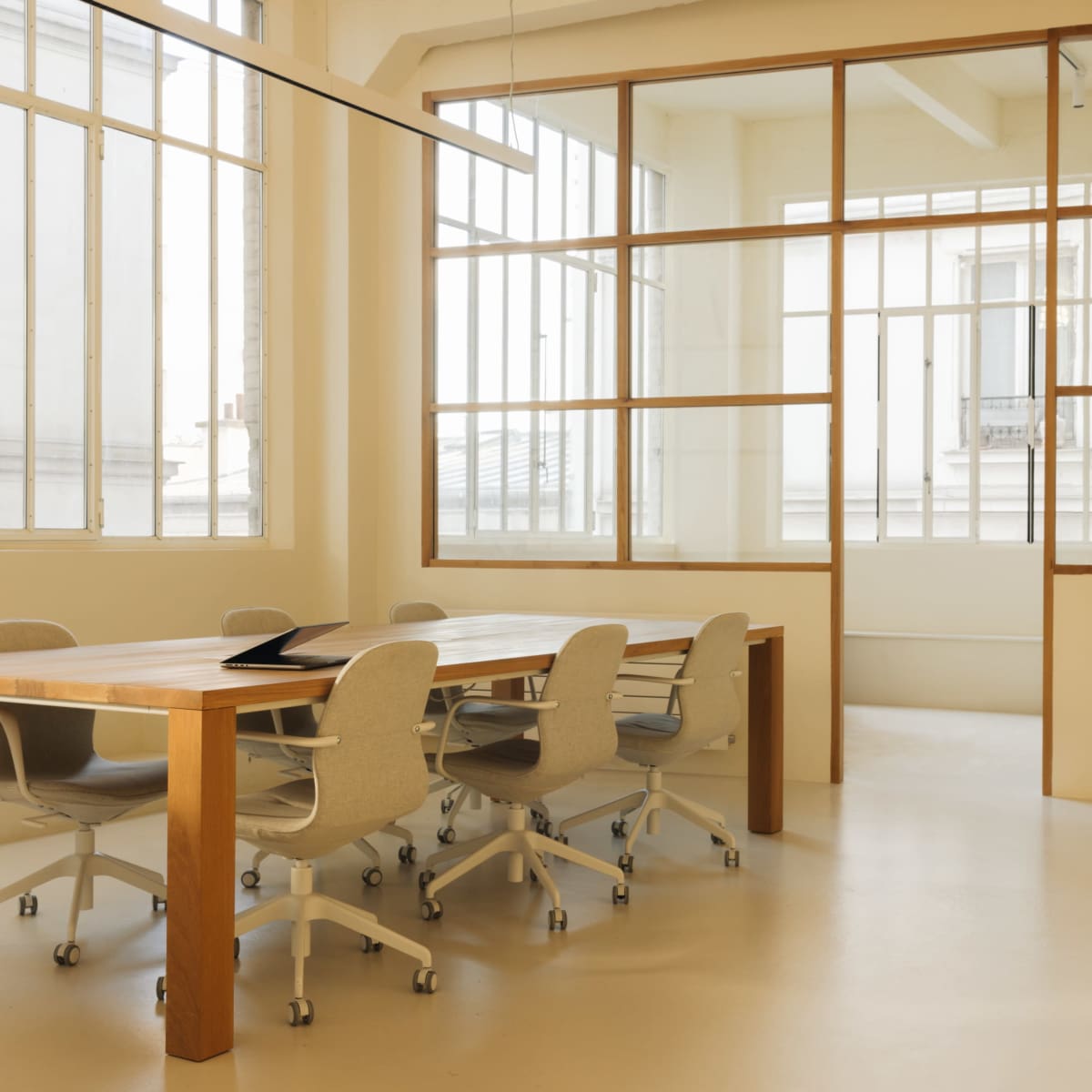A modern conference room features a wooden table surrounded by ergonomic chairs, with large windows allowing natural light to fill the space.