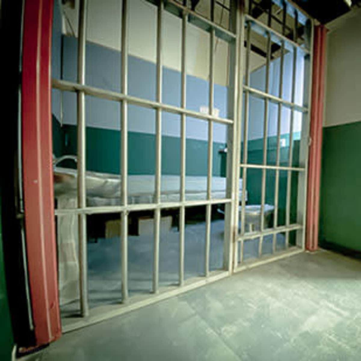 A view of a jail cell with metal bars and a simple bed inside.