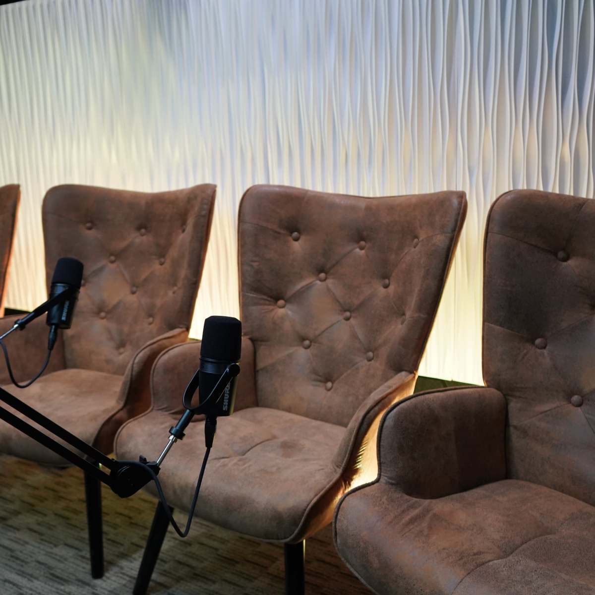 Three microphone-equipped chairs arranged in front of a textured illuminated wall.